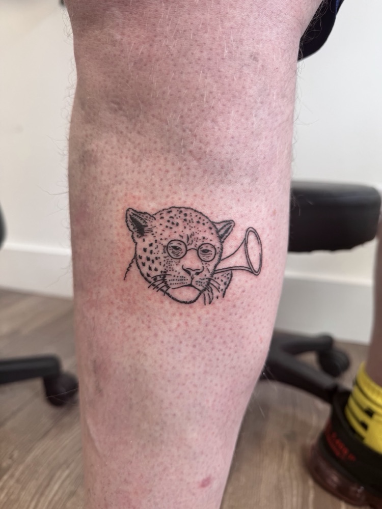 Fine-line illustrative leopard with a trumpet tattoo on a leg