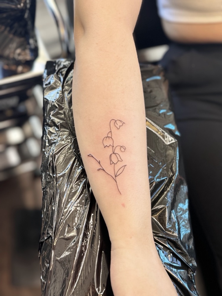 Delicate fine-line lily of the valley tattoo on a forearm